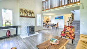 A spacious living room with hardwood floors, a fireplace, a dining area, and a staircase leading to an upper level. - Stunning Hood Canal Getaway w/ Private Deck! (Belfair)