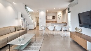 Un salon moderne comprenant un canapé, une table basse et un coin repas avec des chaises. Un escalier mène à un autre niveau.