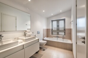 Une salle de bain moderne équipée d’un lavabo, d’un miroir, de toilettes et d’une baignoire.