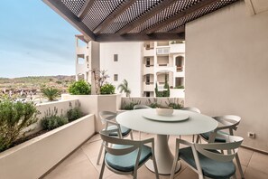 Un balcon avec une table ronde et des chaises, donnant sur un quartier résidentiel avec des immeubles et de la verdure.