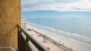 Blick auf einen Strand vom Balkon mit Geländer, ein Sandstrand und ein Gebäude im Hintergrund.
