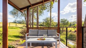 Eine Holzterrasse mit einer weißen Couch und einem Tisch, einem Weinglas und einem Teller Essen.