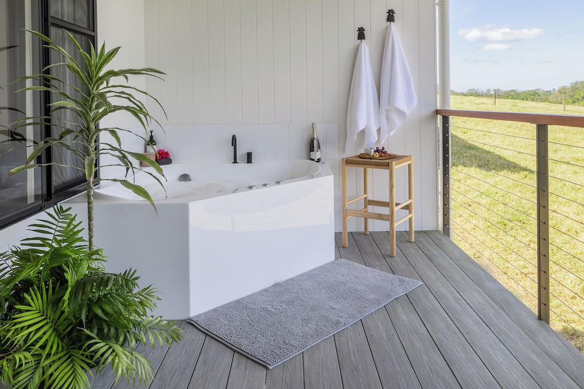 A modern bathroom with a freestanding bathtub, a wooden stool, and a potted plant.