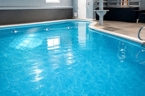 An indoor swimming pool with clear water, a starting block, and a changing room area.