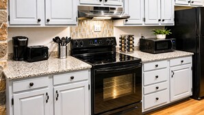 A kitchen with white cabinets, a black stove, an oven, a microwave, and a coffee maker. - Large North Conway Vacation Home Indoor Pool, Pool Table Sleeps 22 (Conway)