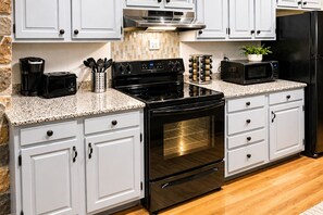 Una cocina con gabinetes blancos, estufa negra, horno, microondas y cafetera.