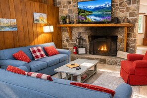 A cozy living room with a stone fireplace, a blue sofa, and a red armchair.