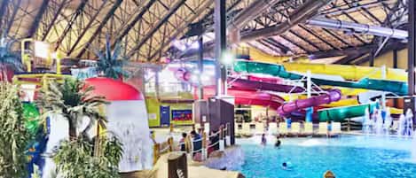 An indoor water park with a large pool, water slides, and palm trees.