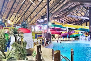Parque acuático interior con una piscina grande, toboganes de agua y palmeras.