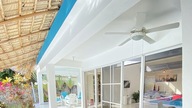 Un espace ext érieur abrité, doté d’une table et de chaises en verre, d’un ventilateur de plafond et offrant une vue sur la piscine.