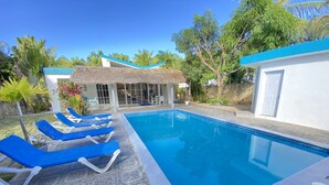 Une piscine avec des chaises longues, une structure à toit de chaume et un mur en pierre.