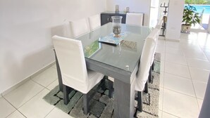 Un espace repas moderne avec une table en verre, des chaises blanches et un tapis à motifs.