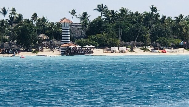 Vista costera con una alta estructura tipo torre, sombrillas de playa y palmeras.