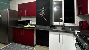 Una cocina con gabinetes rojo y blanco, un extractor de aire negro, un refrigerador de acero inoxidable, un microondas y una estufa.