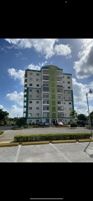 Un edificio de varios pisos con fachada verde y blanca, múltiples balcones y un estacionamiento al frente.