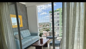 Una sala de estar moderna con un sofá, una mesa de centro y vistas de un paisaje urbano a través de grandes ventanales.