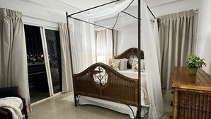 Un dormitorio con cama con dosel, una mesita de noche, una planta en maceta y vistas a través de la puerta de cristal.