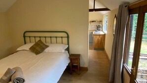 A bedroom with a bed, pillows, a small wooden nightstand, and a window with curtains.