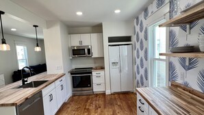 Uma cozinha moderna com piso de madeira, armários brancos, eletrodomésticos de aço inoxidável e iluminação pendente.