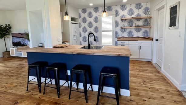 Cozinha moderna com ilha central, banquetas, luminárias pendentes e backsplash estampado.