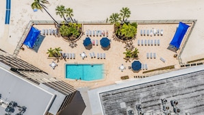 Vista aérea de um hotel com piscina, espreguiçadeiras e palmeiras.