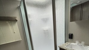 A bathroom with a shower enclosure, toilet, sink, and wooden flooring. - Spacious RV w/ large shower & Queen bed (Pacific)