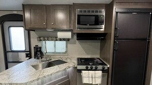 A compact kitchen with a sink, microwave, stove, and refrigerator. - Spacious RV w/ large shower & Queen bed (Pacific)