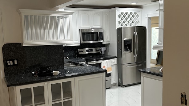 Una cocina moderna con armarios blancos, electrodomésticos de acero inoxidable y piso de mármol.