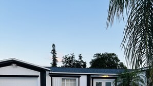 Una casa moderna de dos pisos con garaje, un porche delantero y un pequeño jardín con plantas y un bebedero para pájaros.
