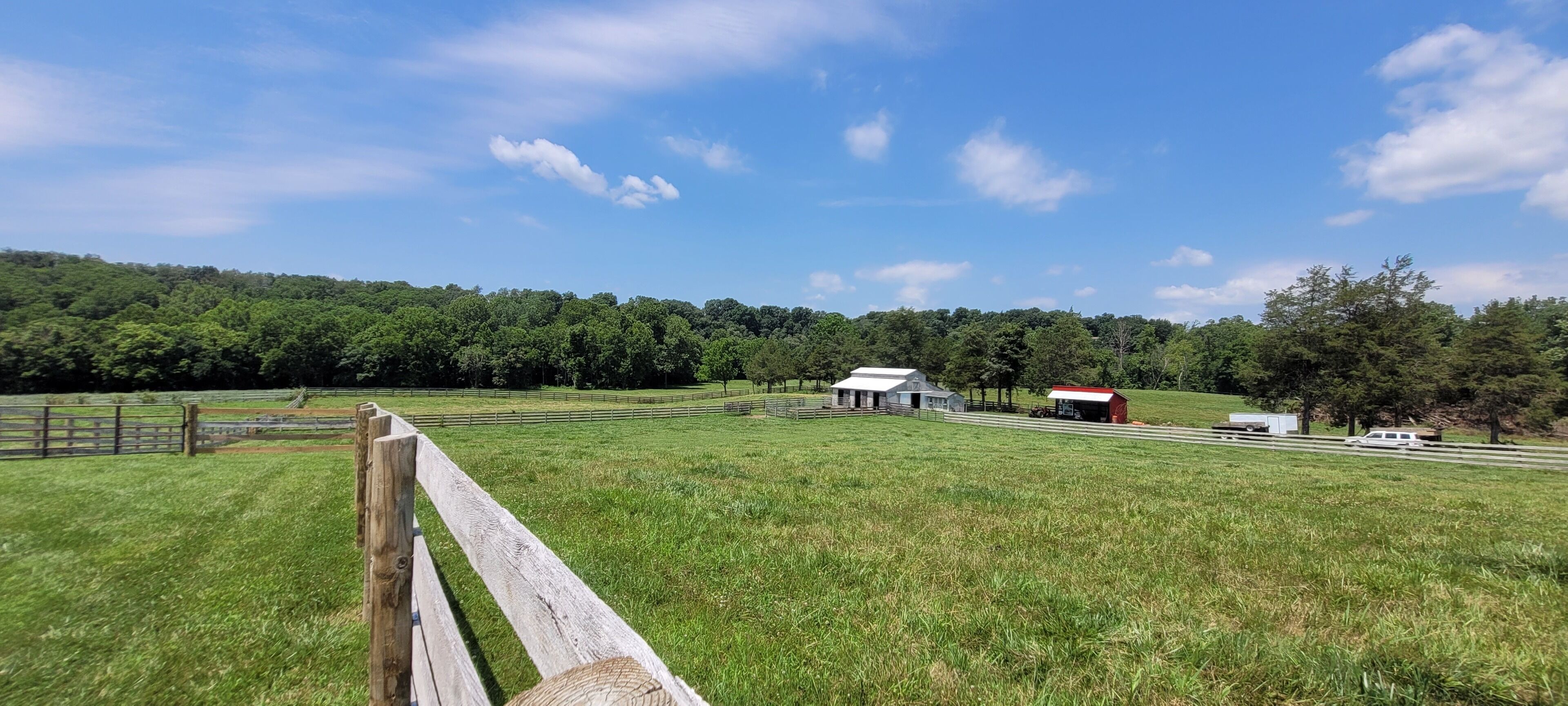Un paysage rural avec un champ délimité par une clôture, un petit bâtiment et un camion.