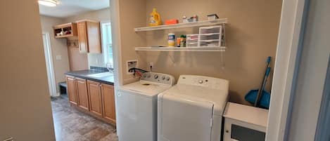 A laundry area with a washing machine, dryer, and shelves with cleaning supplies.