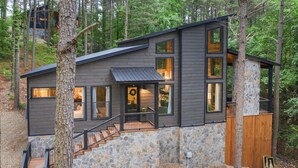 A modern two-story cabin with a stone foundation, large windows, and a wooden deck.