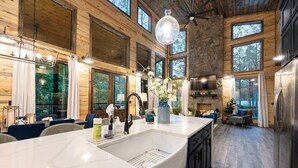 A spacious kitchen with a large island, stone accents, and large windows offering views of the outdoors.