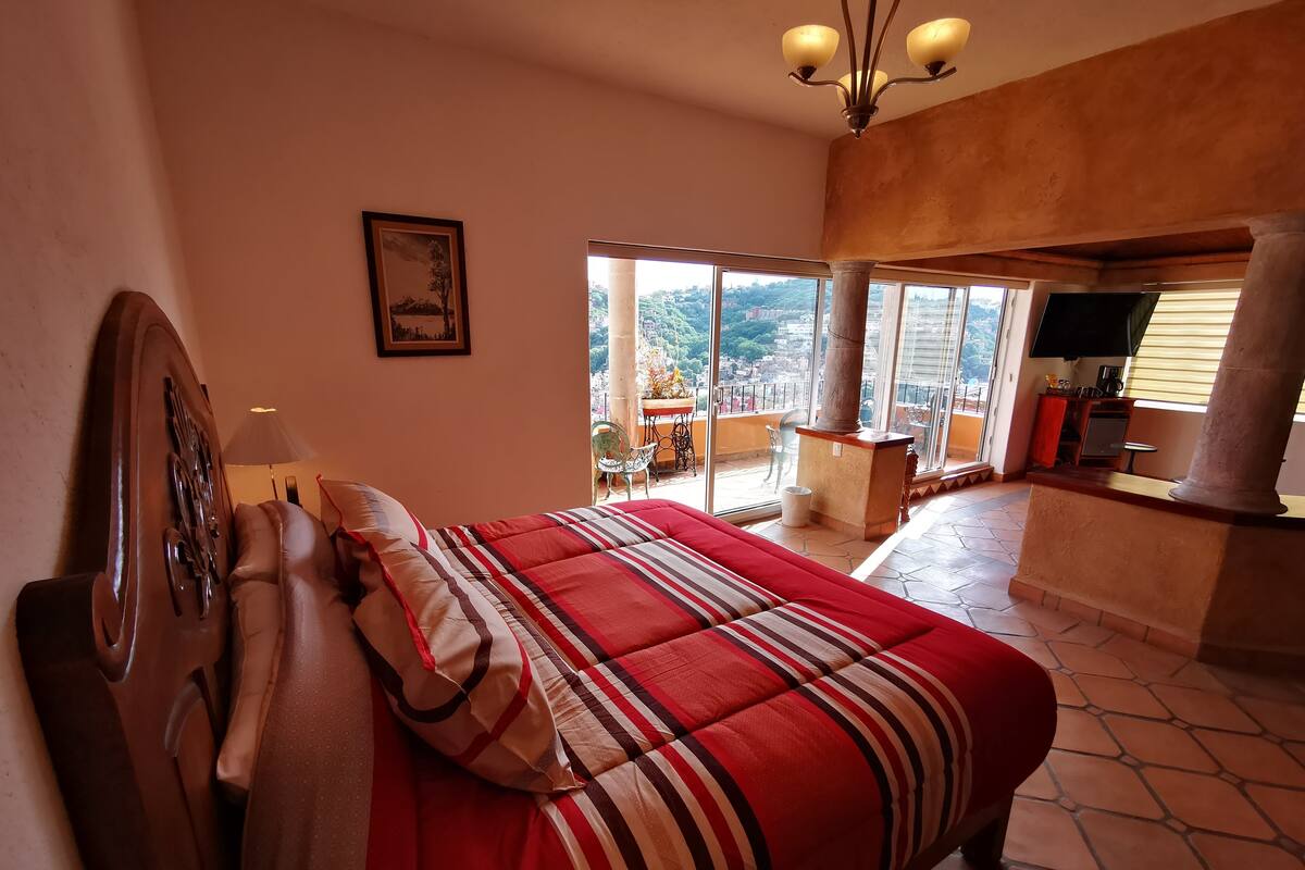 A bedroom with a bed, a wooden headboard, a framed picture, and a balcony with a view.