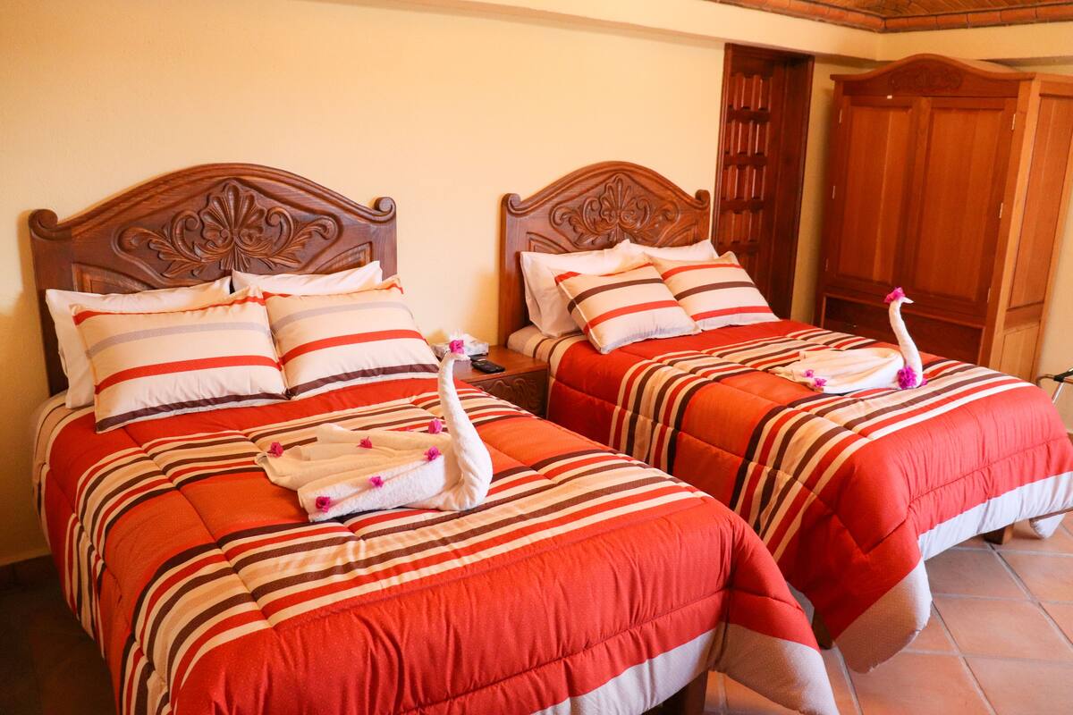 Two beds with striped bedding and decorative swans, a wooden headboard, and a wooden wardrobe.