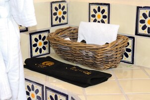Un baño con una cesta de mimbre que contiene una toalla blanca y una toalla negra con bordados dorados.