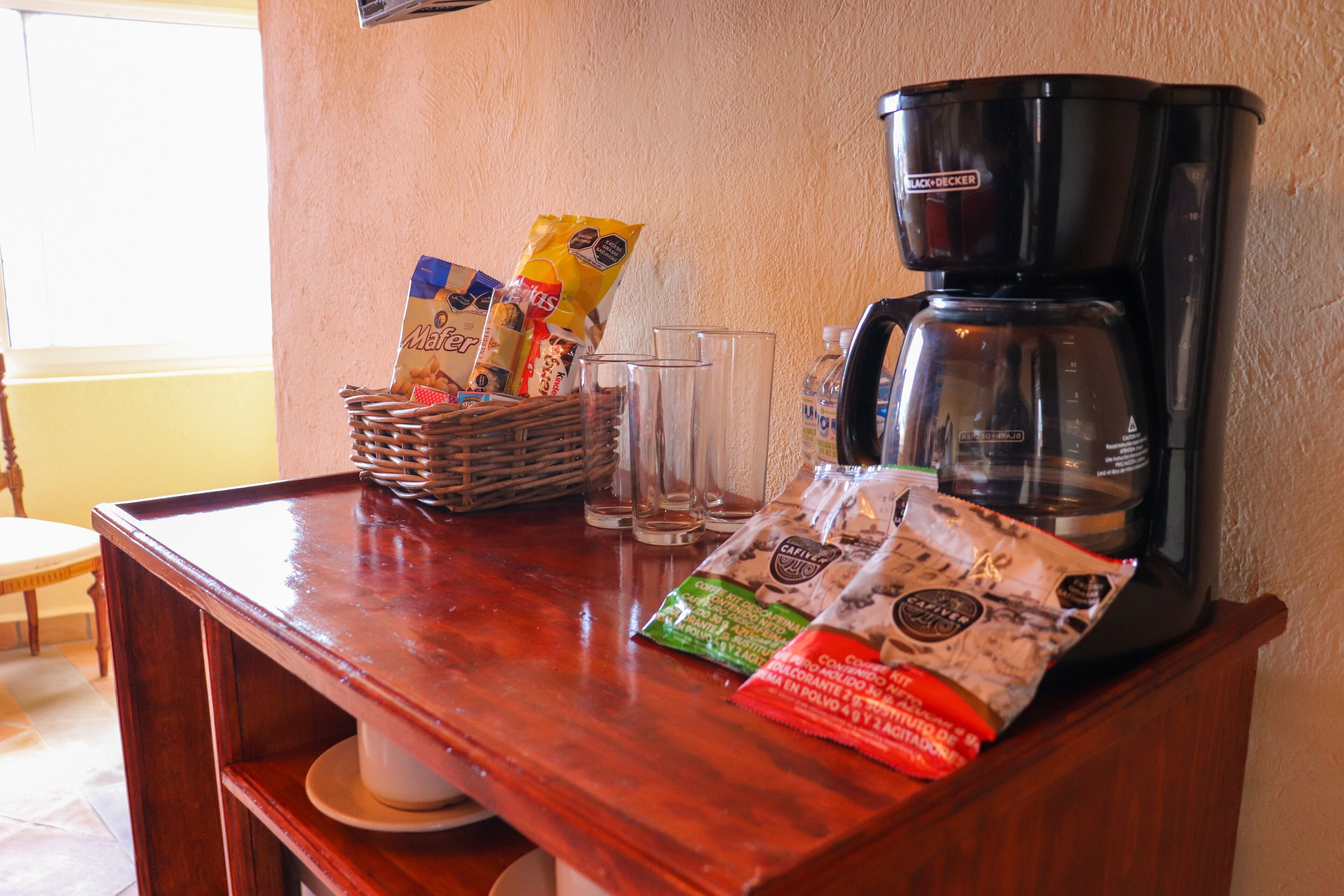 A wooden bar counter with a coffee maker, glasses, and snack bags.