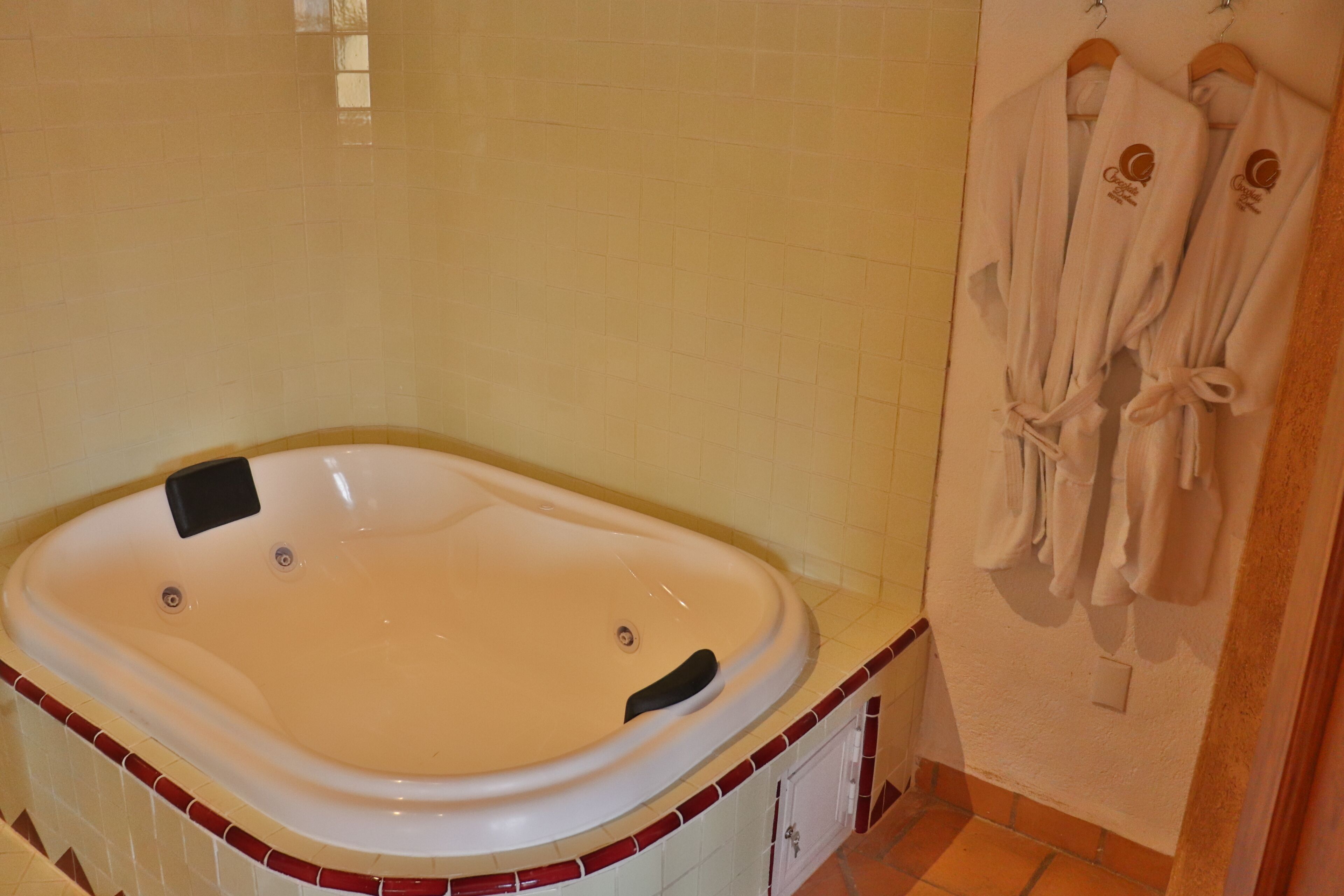 A bathroom with a large bathtub, tiled walls, and a towel rack with robes.