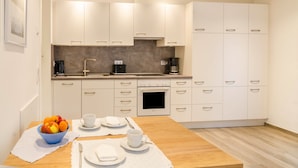 Een moderne keuken met witte kasten, een inbouwoven en een eettafel gedekt met borden, bekers en een schaal fruit.