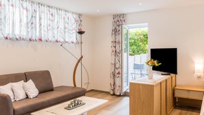Een moderne woonkamer met een bank, salontafel, tv-meubel en uitzicht op groen.