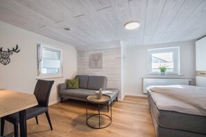 A modern room with a wooden ceiling, a sofa, a small round table, a bed, and a window with a plant.