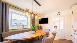 Un comedor con una mesa de madera, sillas acolchadas, lámparas colgantes, una planta en maceta y vistas a través de una ventana.
