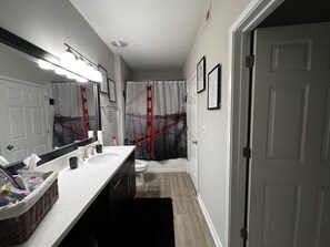 Bathroom features a large mirror, two sinks, and a shower area with a unique shower curtain design.
