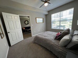 Relax in a spacious bedroom with a large bed, ceiling fan, and window with blinds.