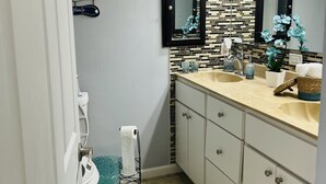 Een badkamer met een betegelde spatwand, een wastafel met spiegel erboven en een handdoekrek met decoratieve voorwerpen.