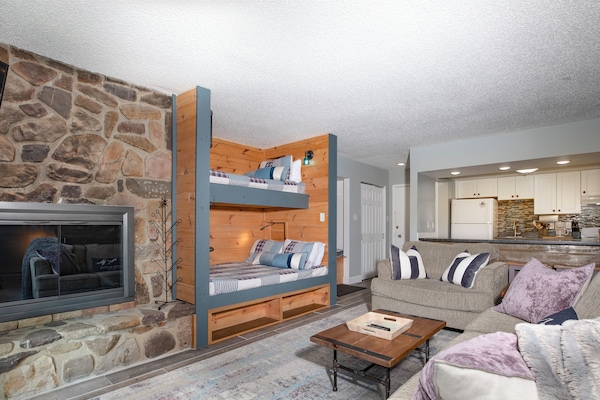 Living room w/ stone fireplace and built-in bunk beds w/ device chargers and reading lamps