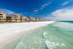 A beachfront hotel with multiple stories, a sandy beach, and clear turquoise waters.