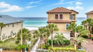A two-story building with a tiled roof, surrounded by palm trees and a pathway leading to the beach. - VILLA ST MARIE: Amazing Water Views ~ Brand NEW Pool! ~  5 Master Suites ~ 1 Row from Private Beach (Destin)