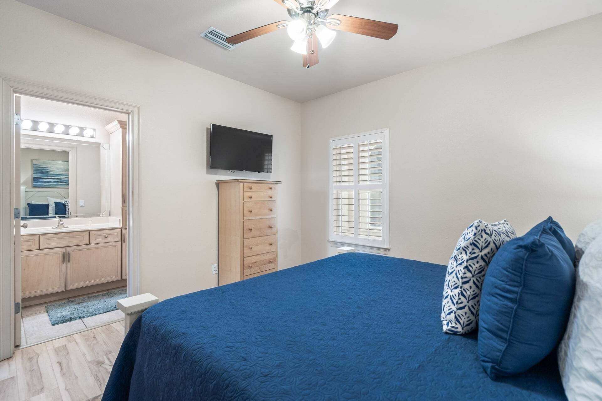 Une chambre à coucher comprenant un lit, une commode, un téléviseur et un ventilateur de plafond.