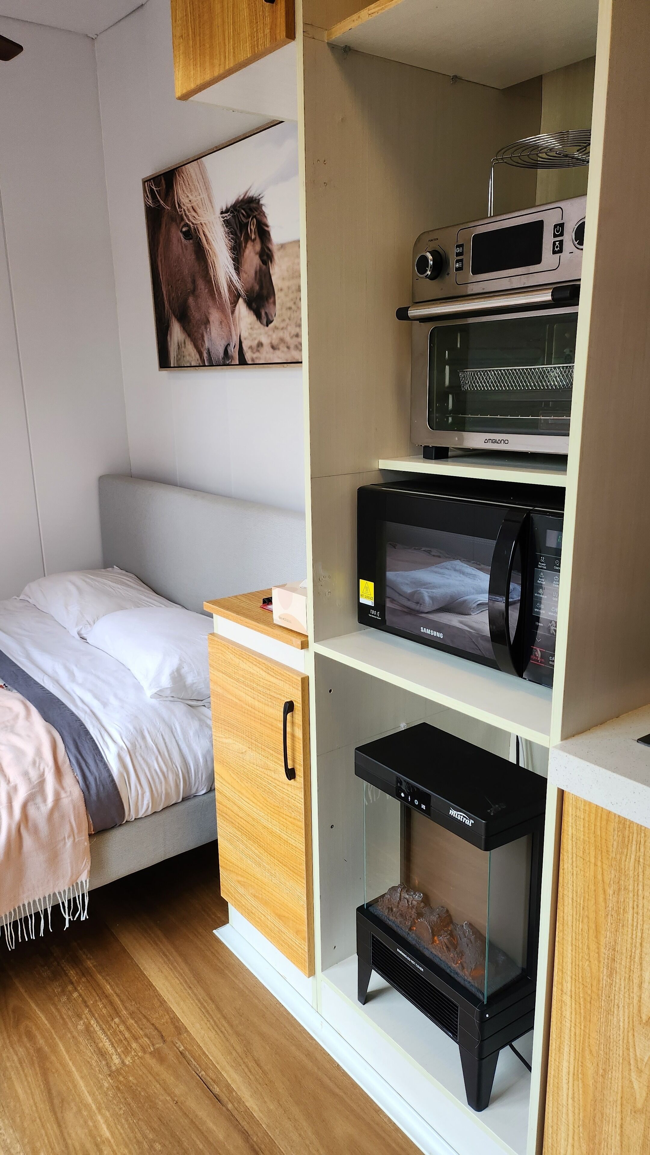 Un dormitorio compacto con cama, un cuadro colgado, microondas y refrigerador pequeño.